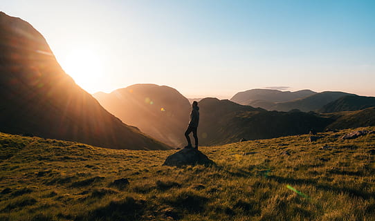 Silhouette Photography of Person Standing on Green Grass in Front of Mountains during Golden Hour HD wallpaper