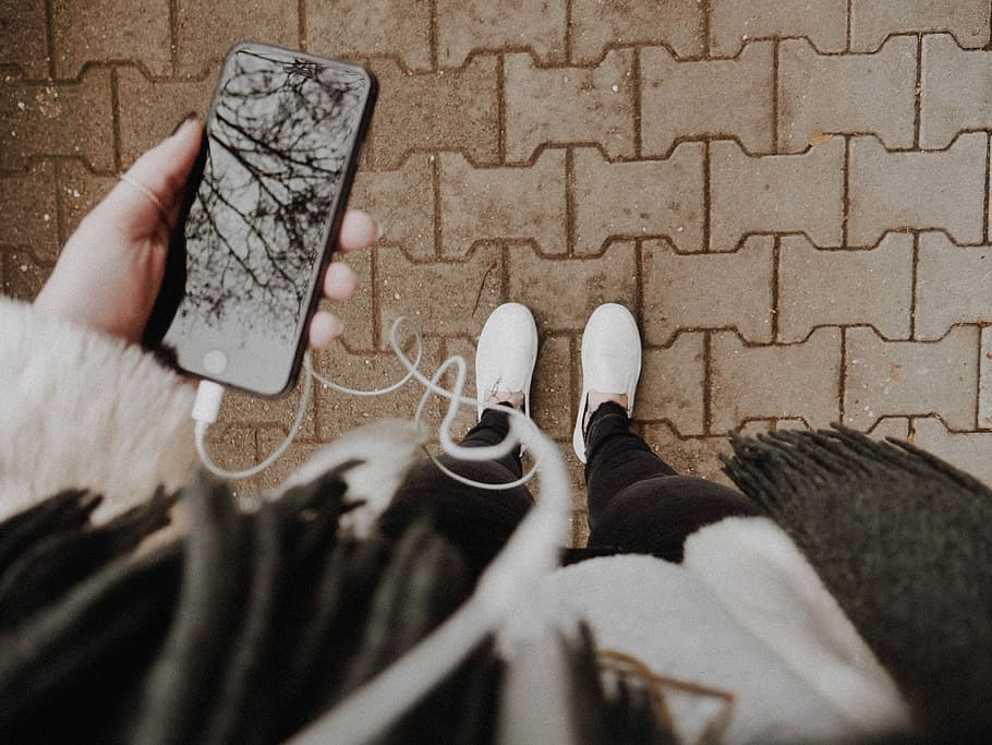 person standing while holding phone, person standing on gray brick pavement while holding black iPhone 7 HD wallpaper