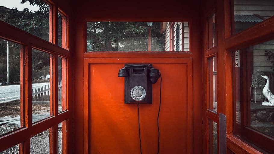 black rotary telephone mounted on red wooden wall, photo of black and red telephone booth