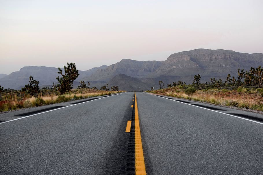 empty road towards mountains, road between grass covered field at daytime