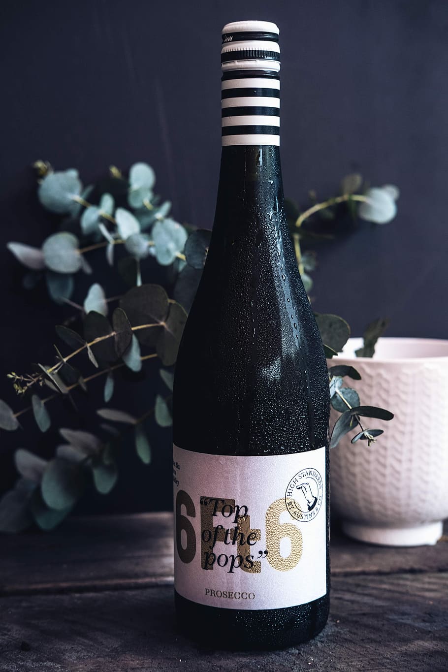 Prosecco wine bottle on table, black wine bottle near vase, eucalyptus