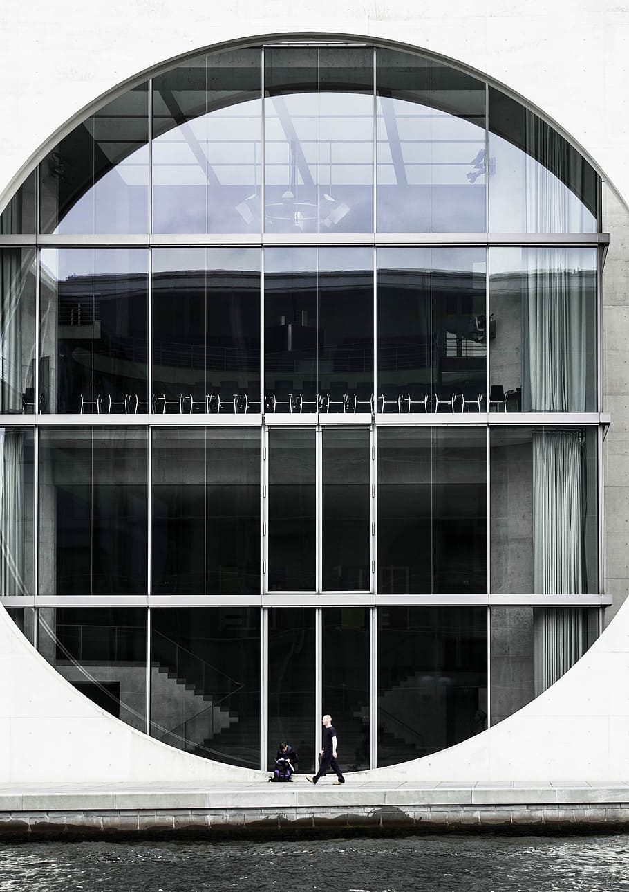 person beside clear glass building, two person standing and sitting in front building during daytime HD wallpaper