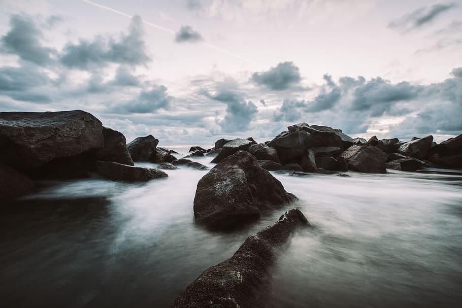 black rocks on river flowing under white and blue sky, body of water with rock formation at daytime HD wallpaper