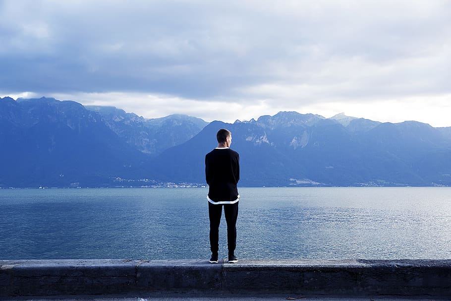 person wearing black pants and top standing on wall, man standing on ledge near body of water, HD wallpaper