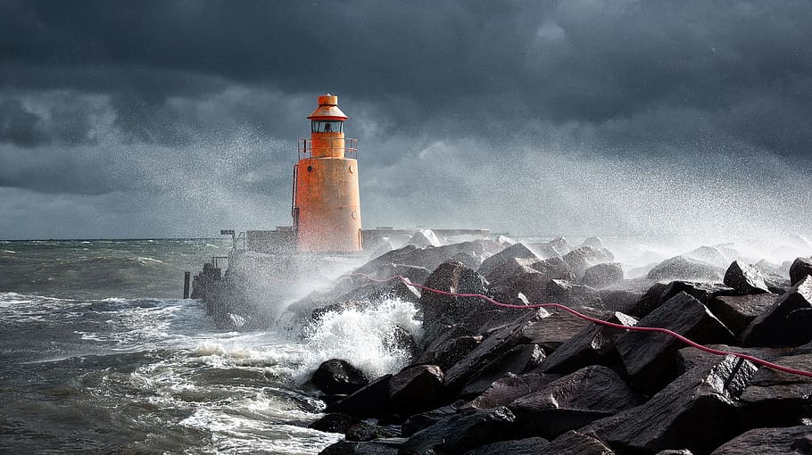 orange lighthouse on rock, rough waves splashing through orange lighthouse photo