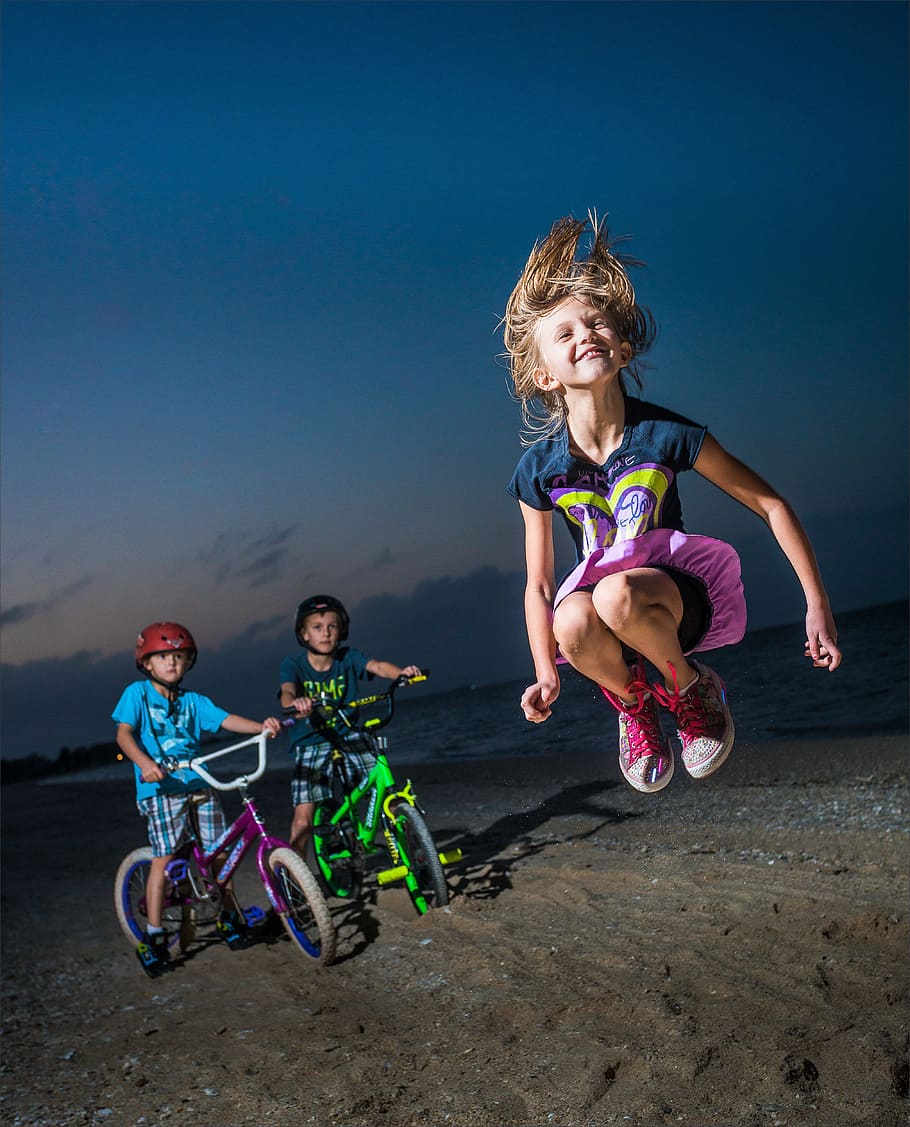 two boy's on bike and girl jumpig on seashore at night time, fun, HD wallpaper