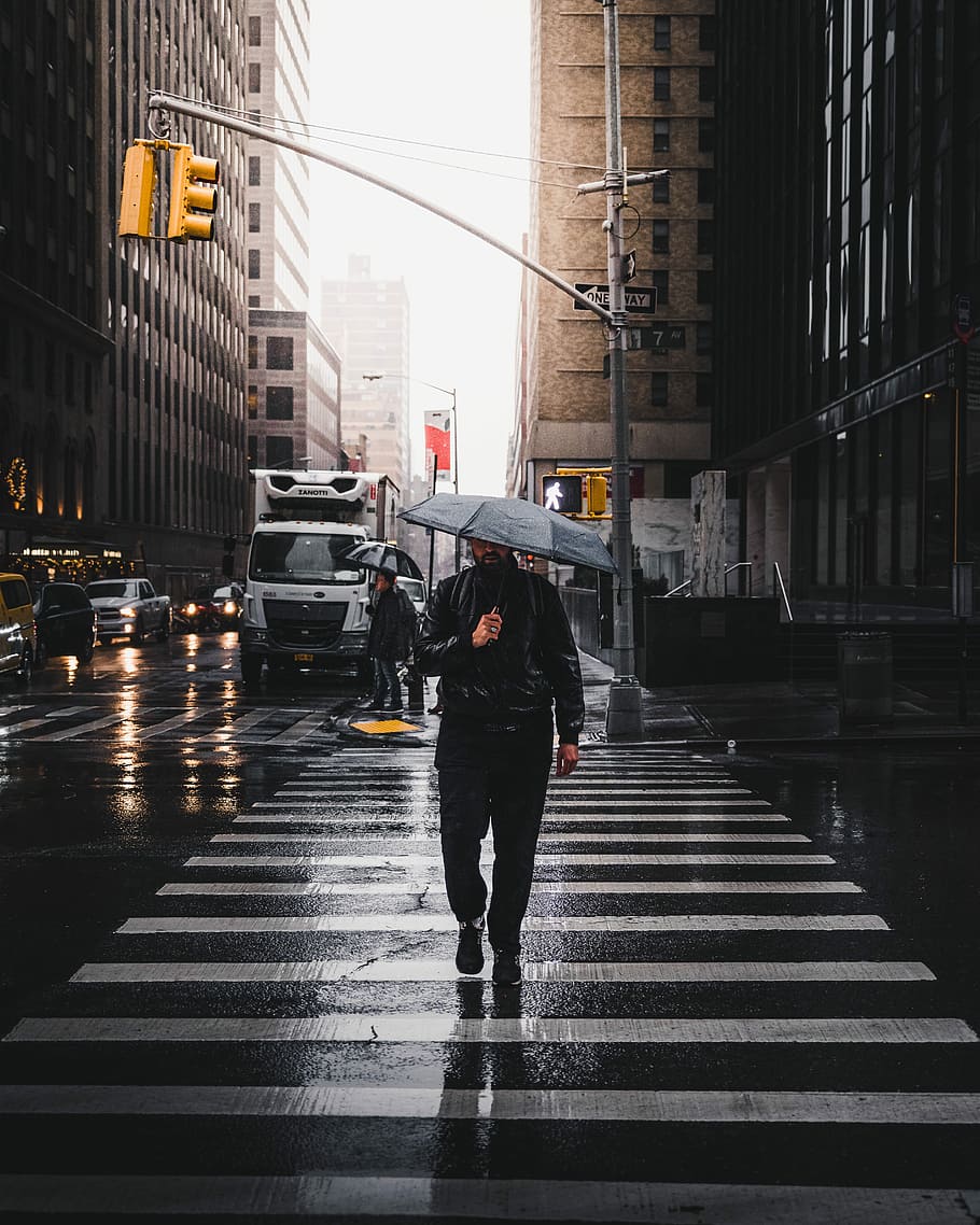 man holding umbrella walking on pedestrian lane, person walking on pedestrian lane while holding umbrella