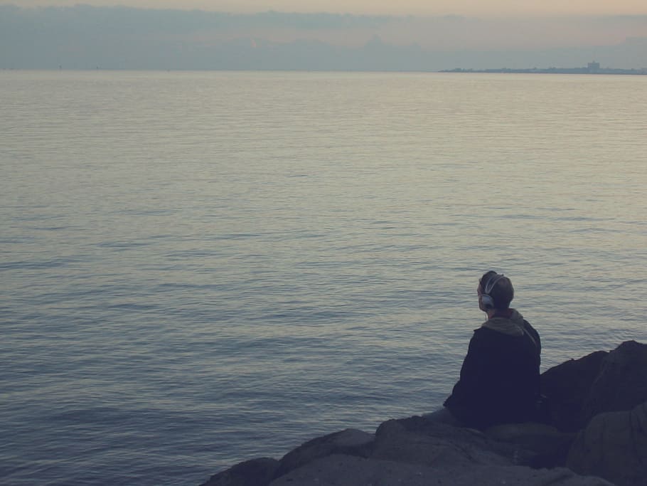 man sitting on rocks near body of water, guy, headphones, coast, HD wallpaper