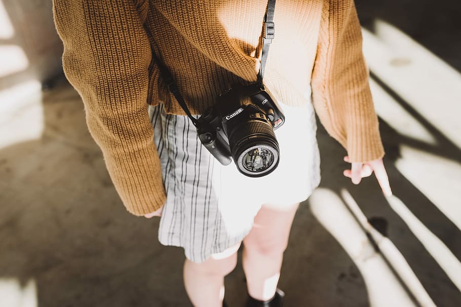 woman wearing brown sweater and white shorts with black Canon DSLR camera sling on her body, woman standing on gray concrete ground HD wallpaper