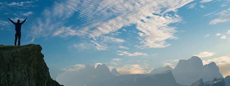silhouette person standing on cliff while raising both hands HD wallpaper