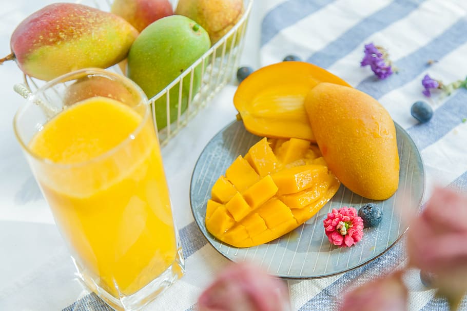 three mangoes and filled pint glass on white and blue striped table