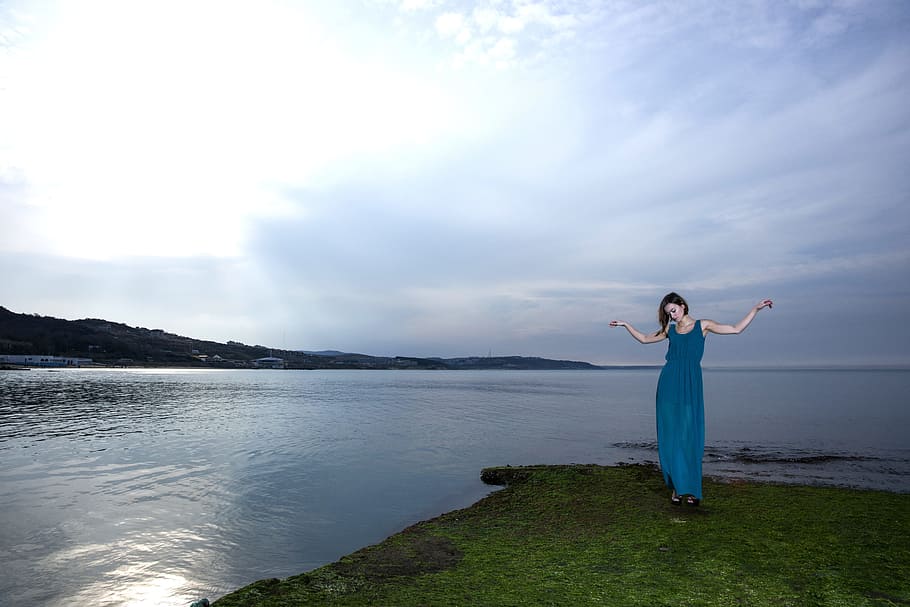 woman in blue long dress standing beside the body of water HD wallpaper