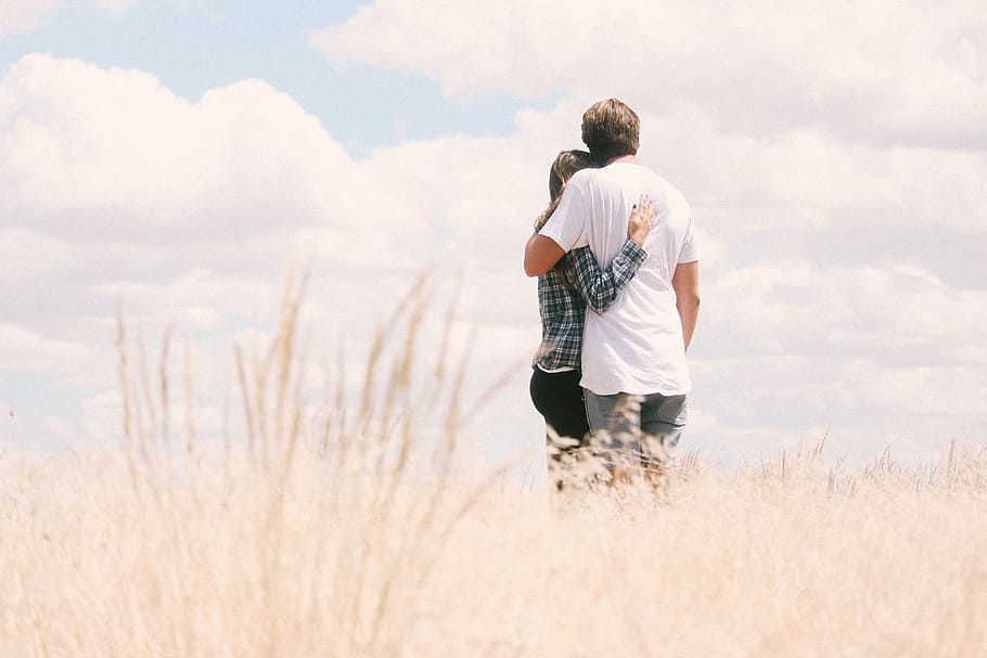 hugging man and woman standing on wheat field during daytime