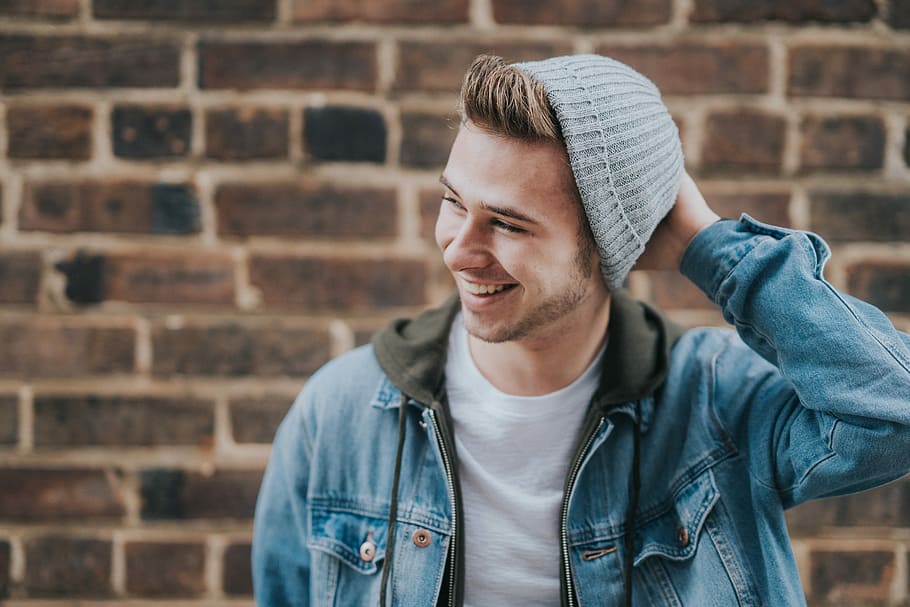 man holding the back of his head while smiling near brick wall, man smiling white holding head HD wallpaper