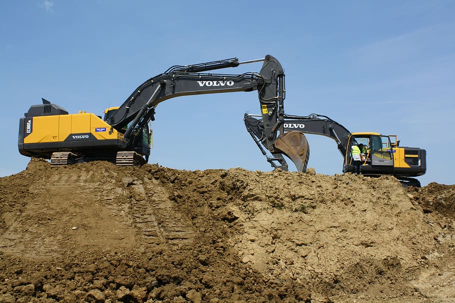 two yellow-and-black Volvo excavators on brown sand under blue sky