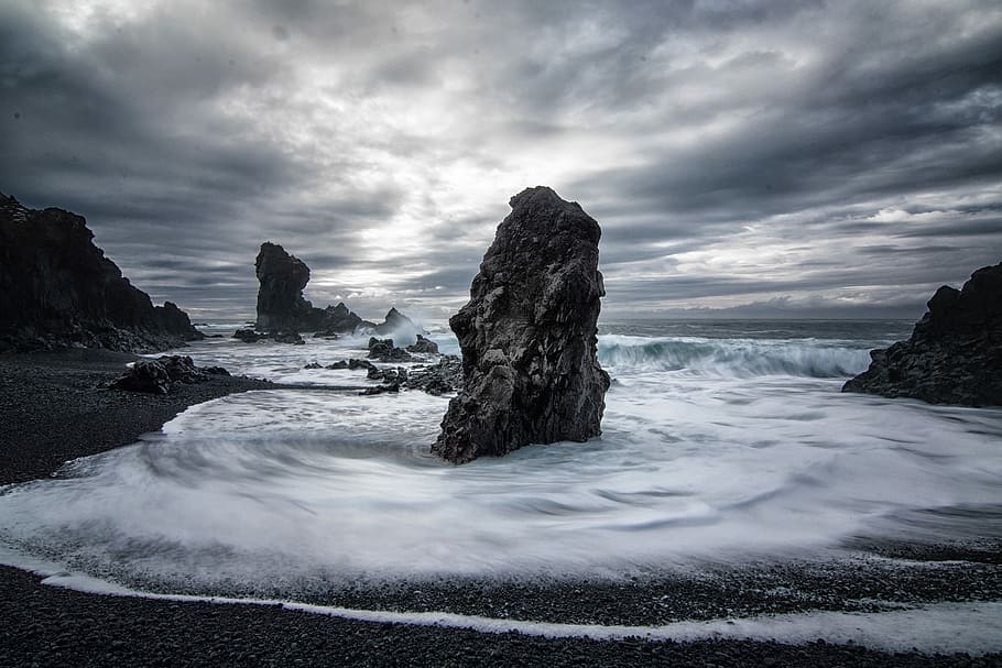 stony beach during cloudy day, grayscale photography of rock formation on body of water HD wallpaper