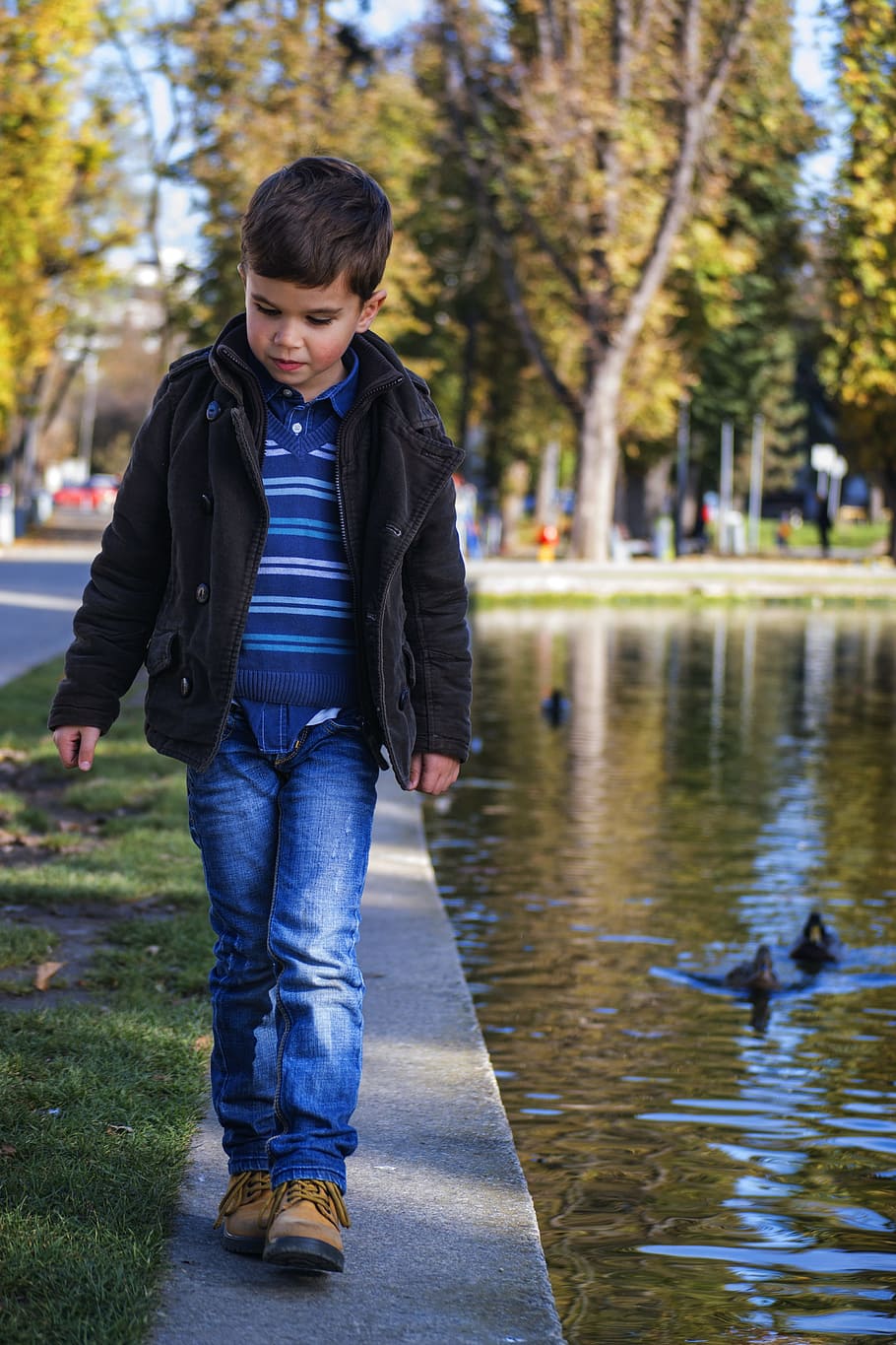 boy in blue and white stripe polo shirt and blue denim jeans walking near body of water