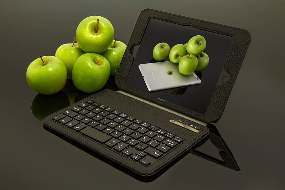 black tablet compute with keyboard besides green apples, apple ipad