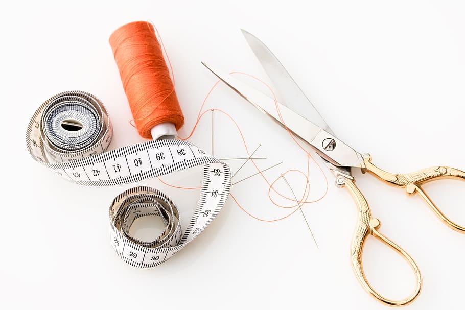 brass and stainless steel scissors beside orange thread, tape measure