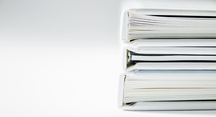A stack of thick folders on a white surface, pile of three white softbounds
