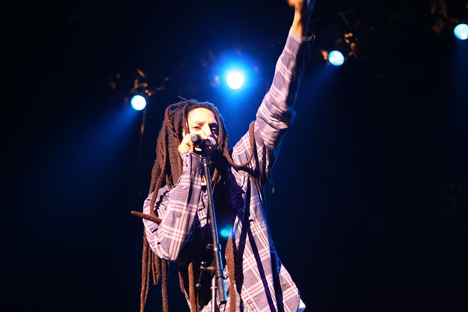 dread-lock haired man standing holding microphone on stage HD wallpaper