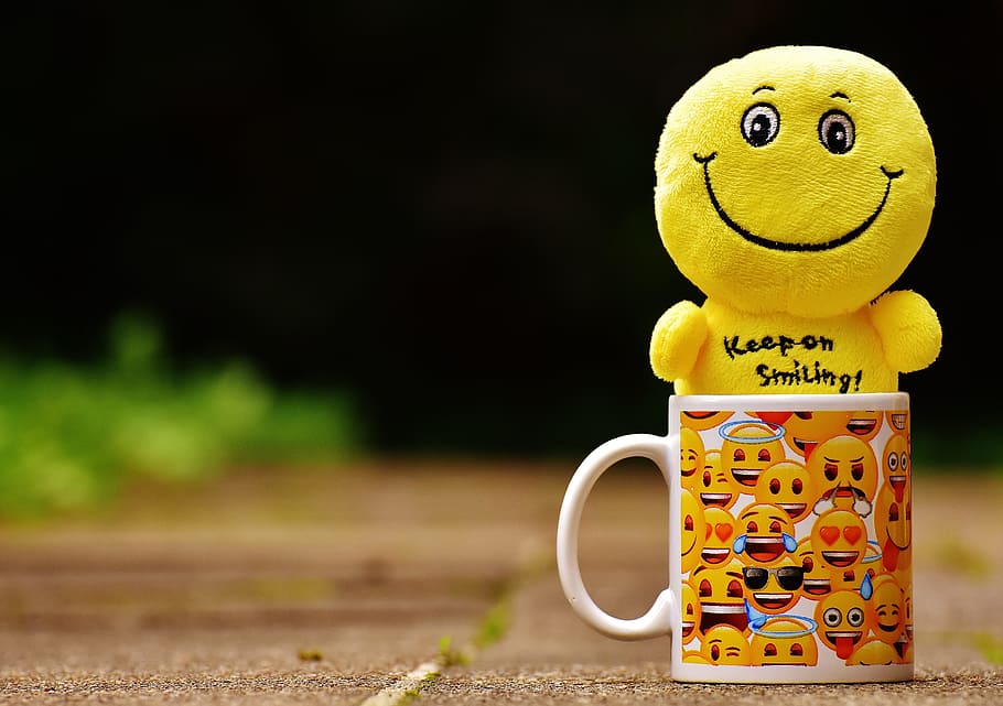 yellow smiley plush toy on mug on brown floor at daytime, smilies