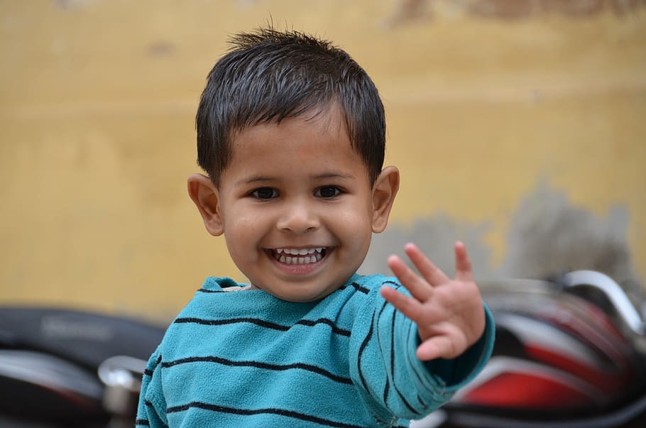 boy wearing blue and black striped sweater reaching and smiling selective-focus photography HD wallpaper