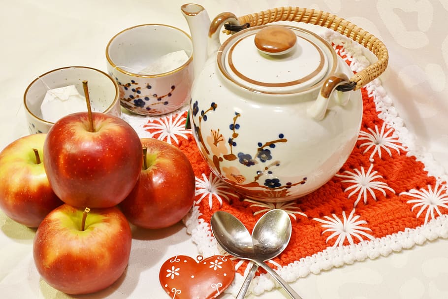 three honeycrisp apples beside white floral teapot and cups, tee