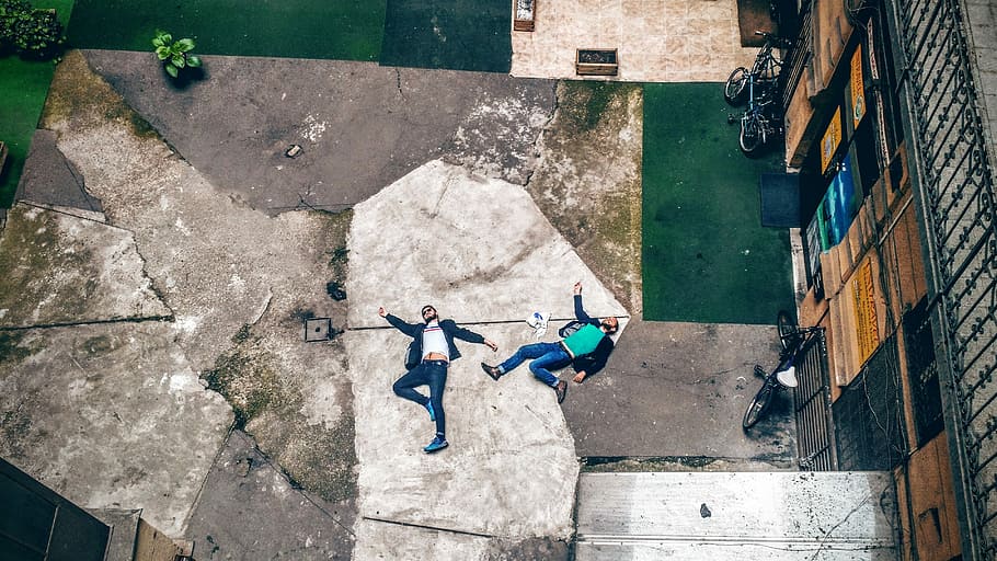 aerial photo of two men lying at white and gray concrete floor in front of brown building during daytime HD wallpaper