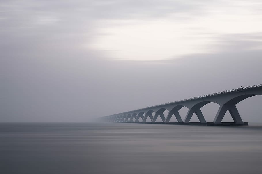 conjunction bridge under white sky, gray metal bridge in sea during foggy day