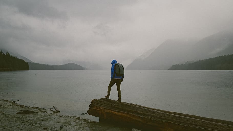man standing on wooden platform in front of water during daytime, person standing on log beside seashore under white cloudy sky at daytime HD wallpaper