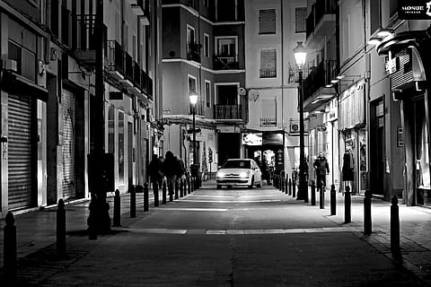 grayscale photo of white car passing on isle surrounded buildings HD wallpaper