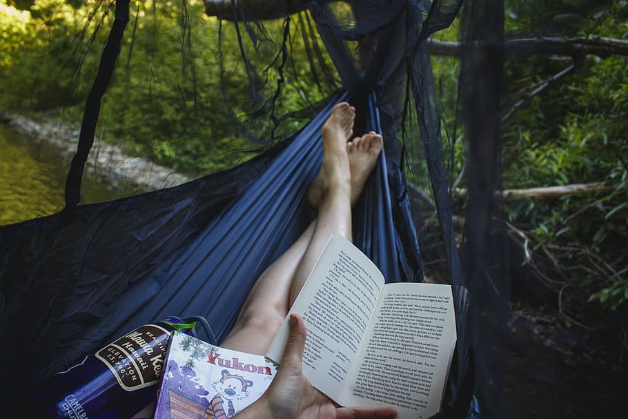 person holding book, person laying on hammock while reading book during daytime HD wallpaper