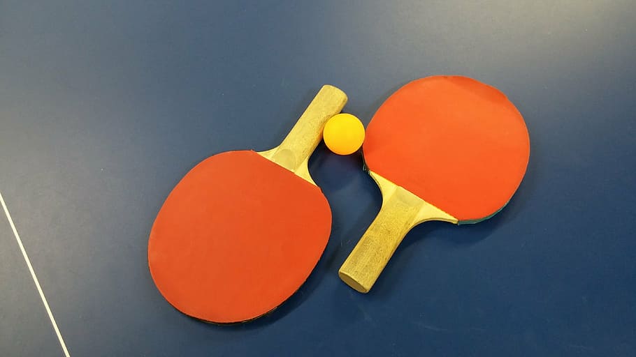 pair of red-and-brown ping-pong paddles on blue surface with yellow ping-pong ball