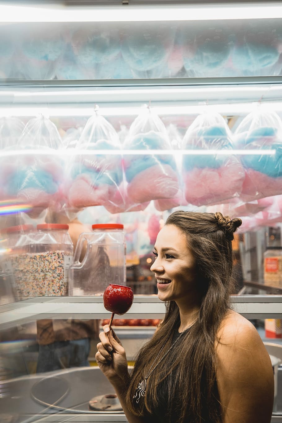 woman holding red apple while smiling, woman holding candied apple near store