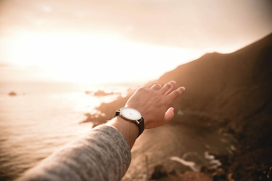 left person's arm wearing watch pointing body of water, person raising hand during golden hour HD wallpaper