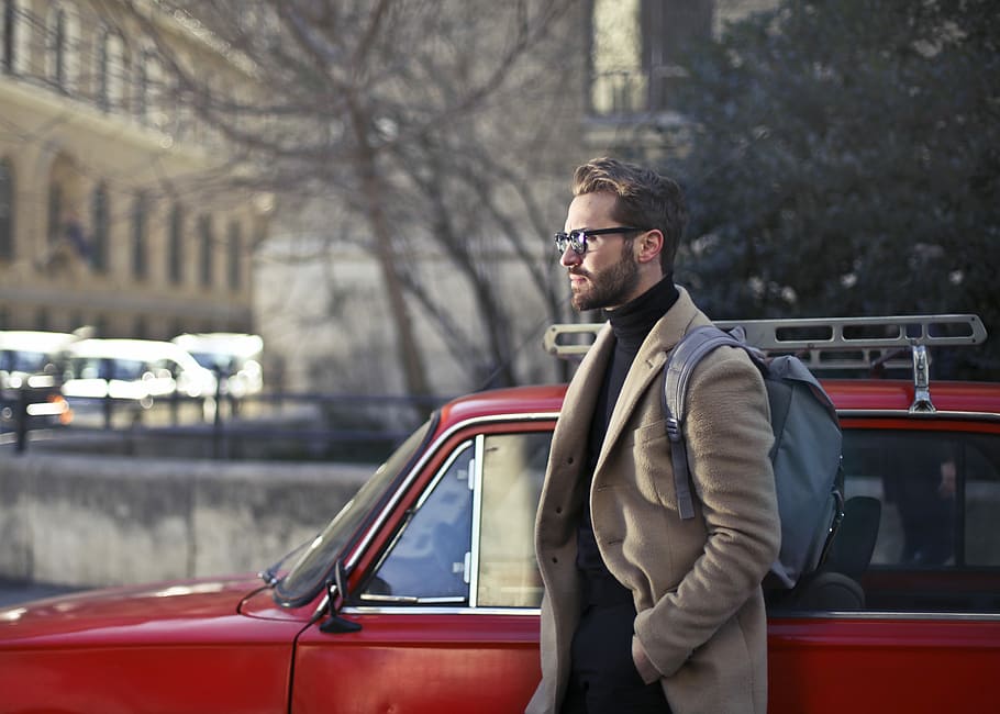 man on beige coat standing beside red car, man wearing brown trench coat beside red car during daytime HD wallpaper