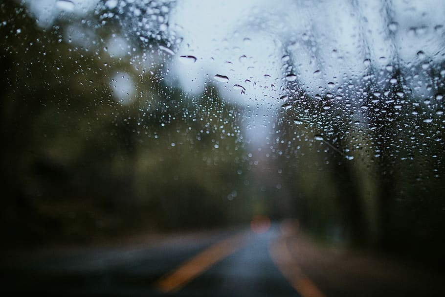 clear glass shrouded with droplets, winding road view through wet glass