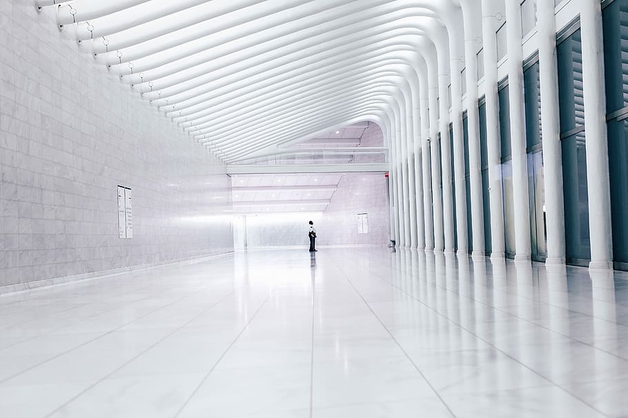 person at end of lobby facing columns, photography of man standing on white ceramic tiles in museum hallway HD wallpaper