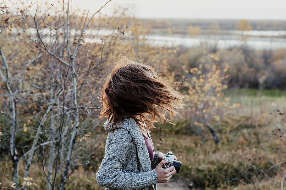 photo of woman waving her hair while holding camera, selective focus photography of woman holding black camera on grass field HD wallpaper