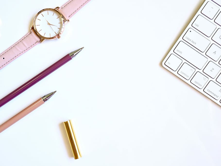 pink pen on table with round gold-colored analog watch, two purple and brown ballpoint pens