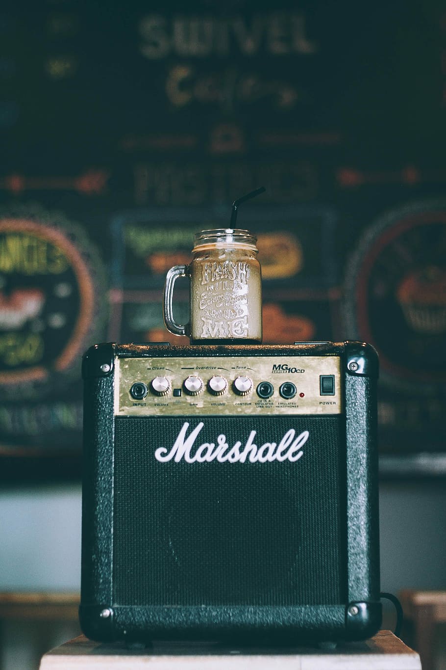 black Marshall guitar amplifier with glass mug on top filled with beverage, clear glass mason jar with coffee on black Marshall guitar amplifier