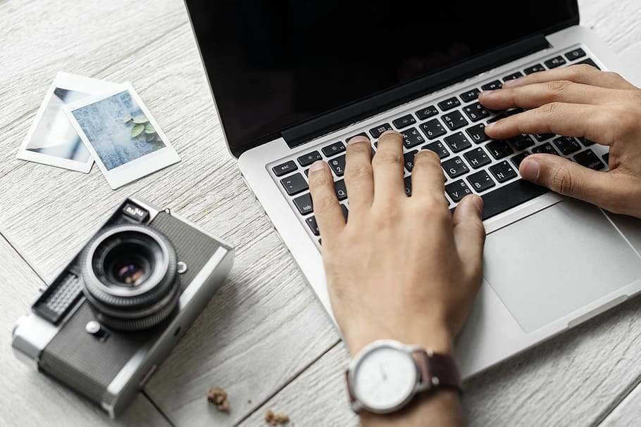 person typing on laptop beside gray camera on white table, workspace HD wallpaper