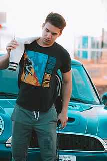 man standing in front gray car, man wearing black t-shirt holding white jacket near blue Mini Cooper HD wallpaper