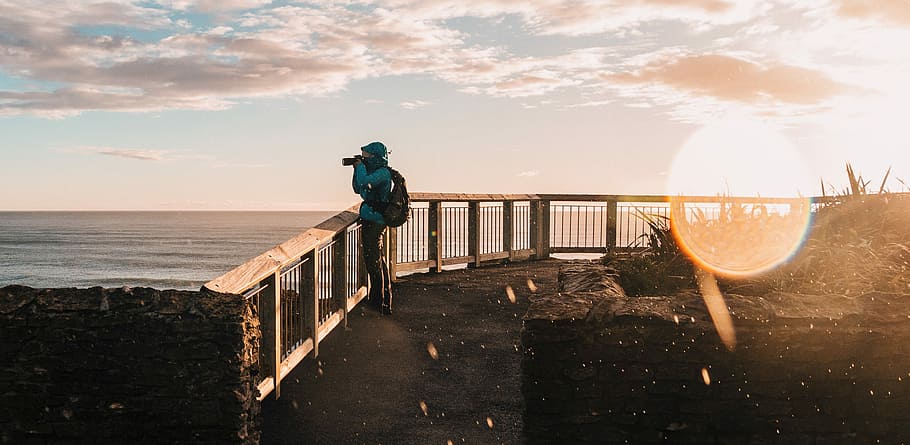 man holding camera, person standing beside fence while taking a photo HD wallpaper
