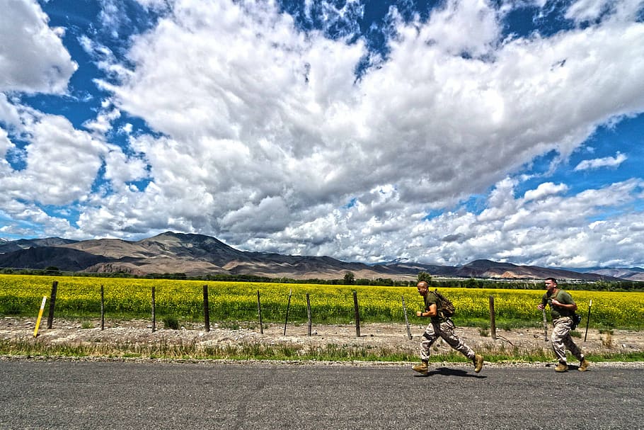 two soldiers running beside grass field and mountain range at daytime HD wallpaper