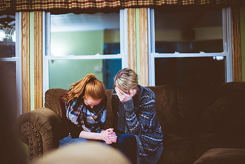 two women holding each other's hand while sitting on brown sofa inside room HD wallpaper