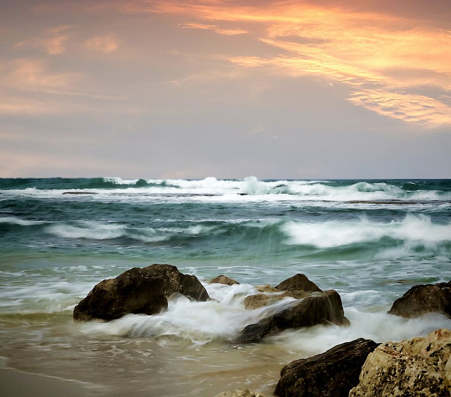 ocean waves bashing rocks on sea shore at sunset, stones, beach