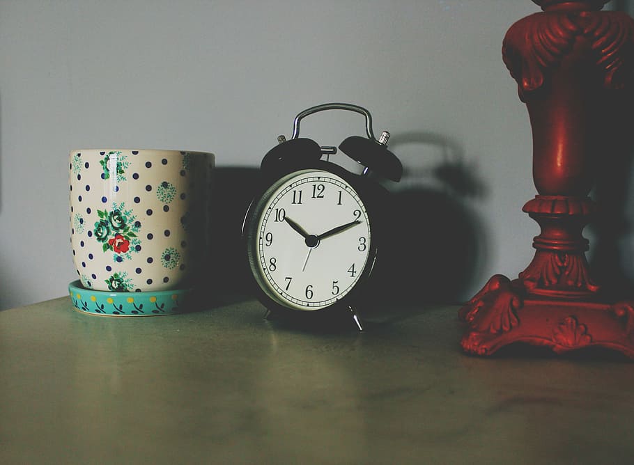 black table clock beside ceramic vase, black alarm clock on brown wooden table