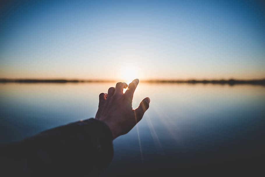 landscape photography of person's hand in front of sun, left human hand during daytime